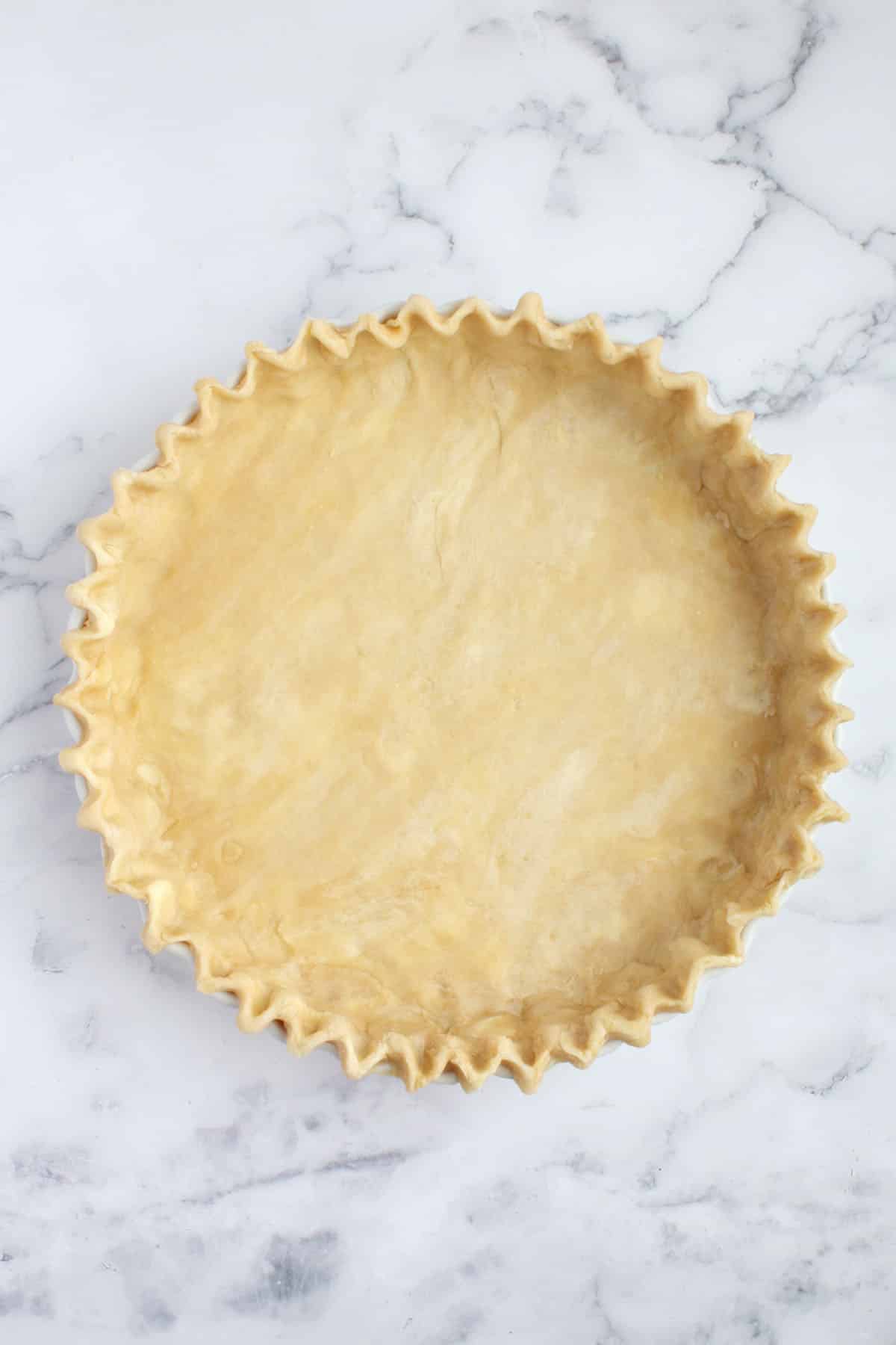 Fluted all-butter pie dough in a white pie plate. 