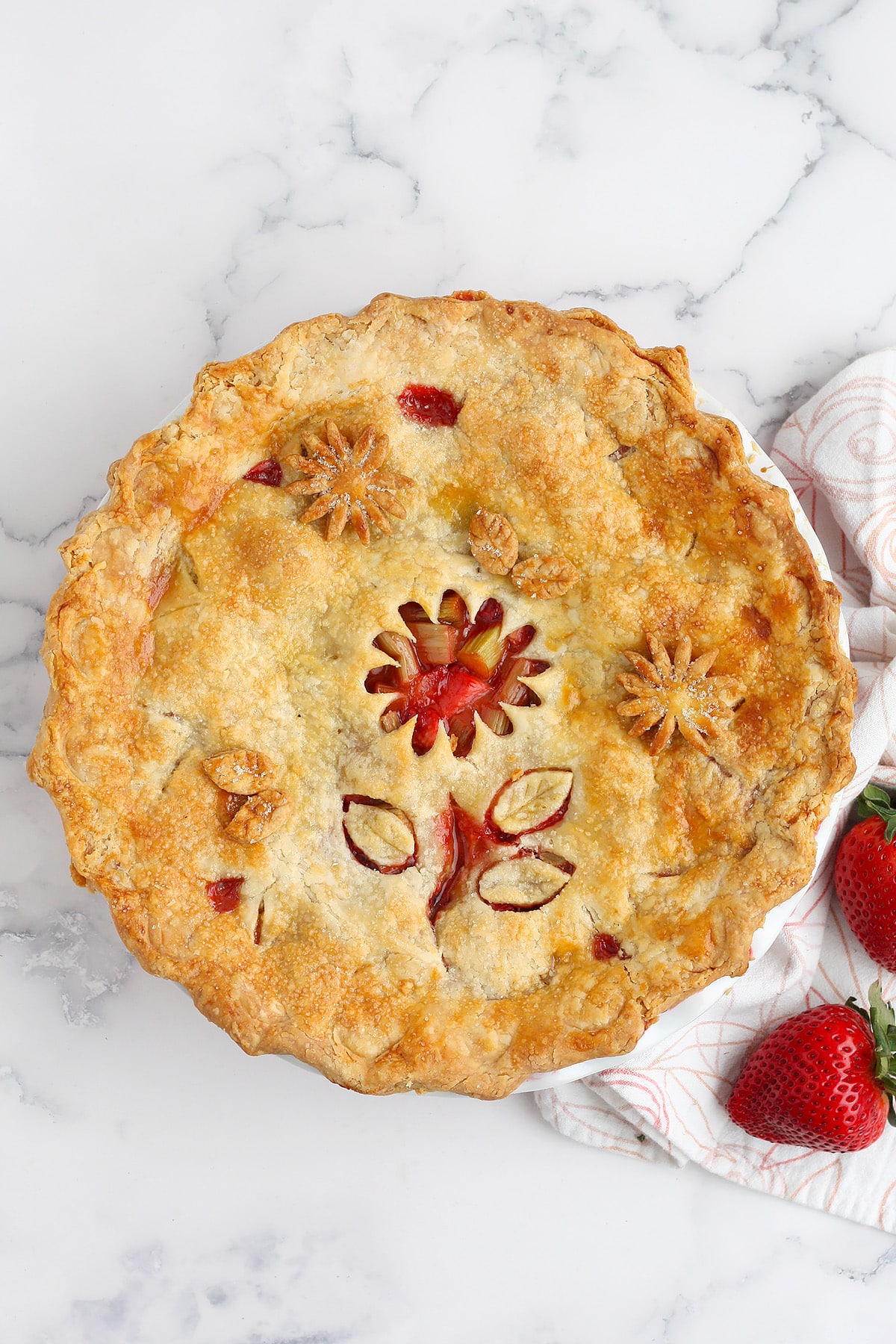 Strawberry Rhubarb Pie in a ceramic pie plate with decorative flower cut outs in the top crust. 