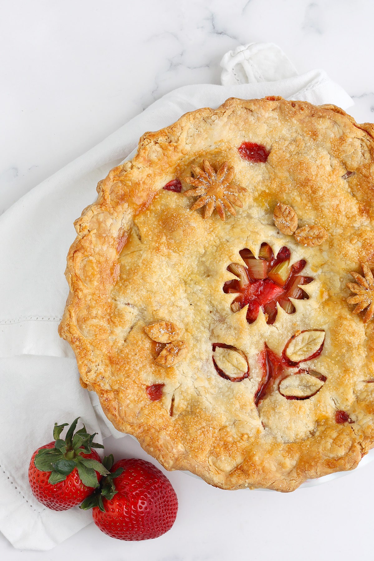 An overhead shot of strawberry rhubarb pie with a flower cutout design. 