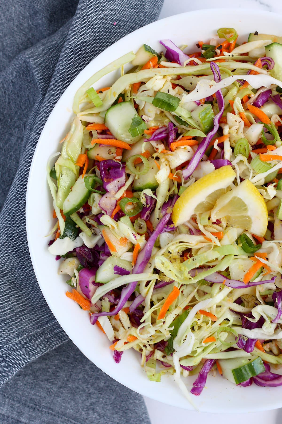 Homemade coleslaw with lemon vinaigrette in a white serving bowl with a blue linen in the background.