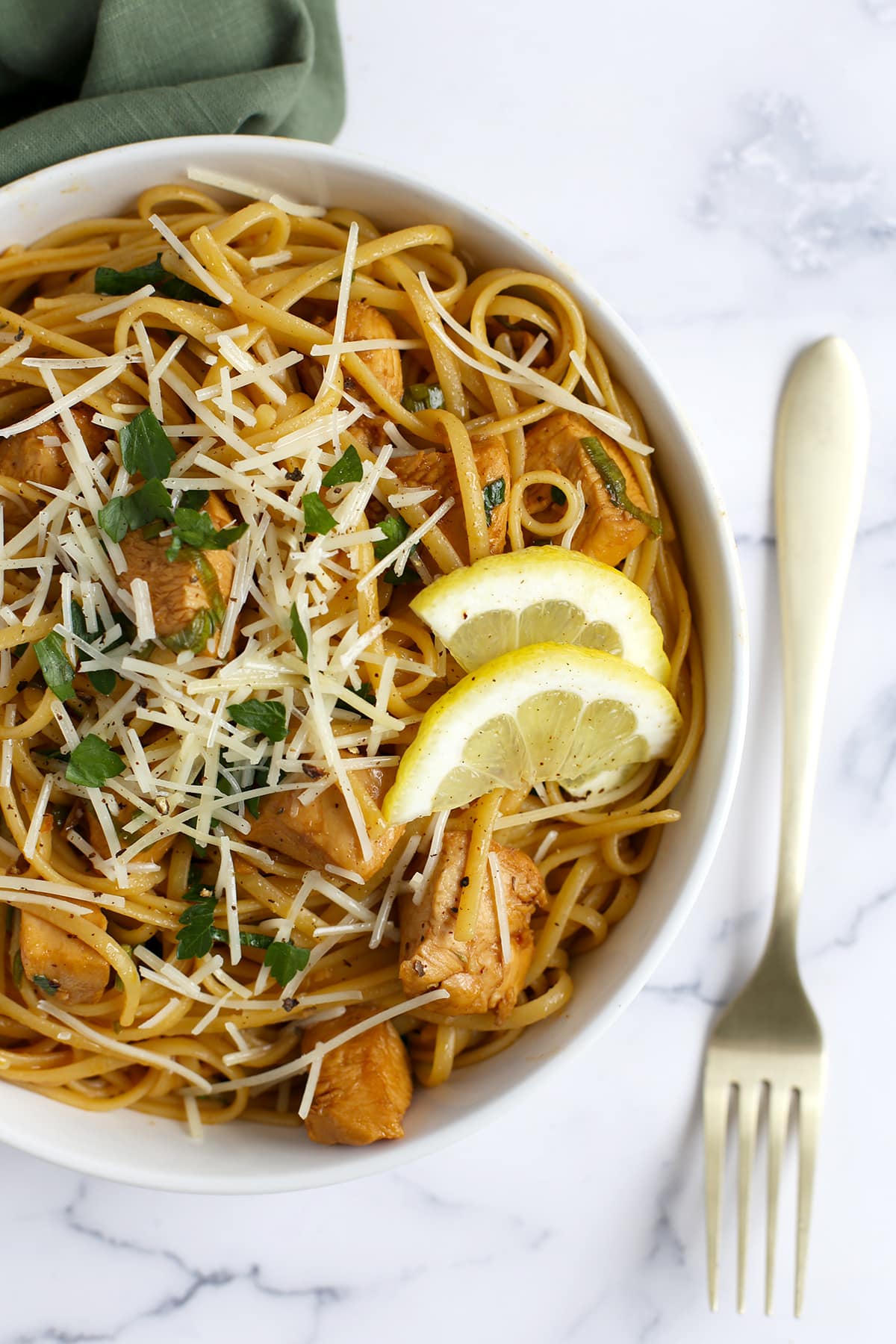 Pasta and chicken topped with shredded parmesan, fresh parsley, and lemon slices in a white serving bowl.