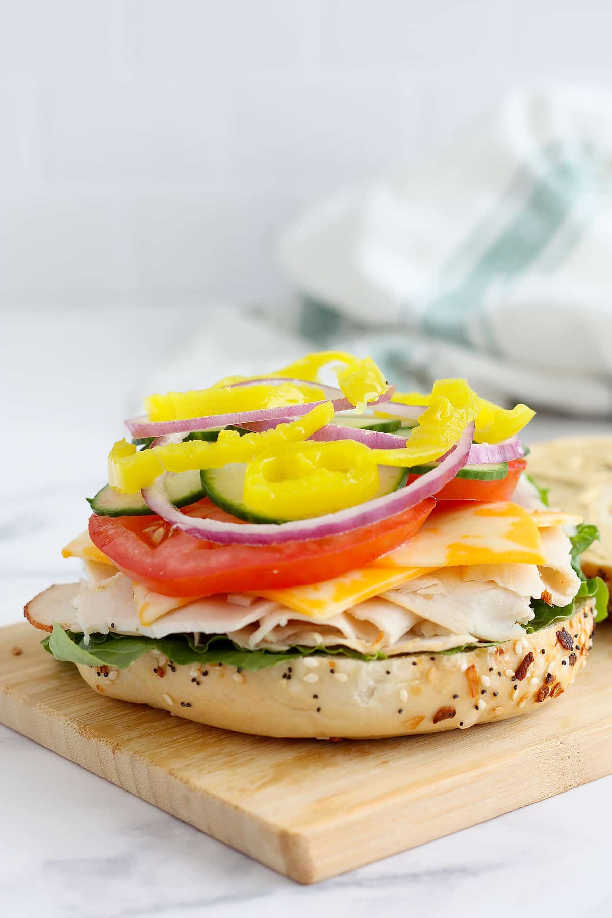 Half of a bagel topped with lettuce, turkey, cheese, and vegetables on a wooden cutting board. 