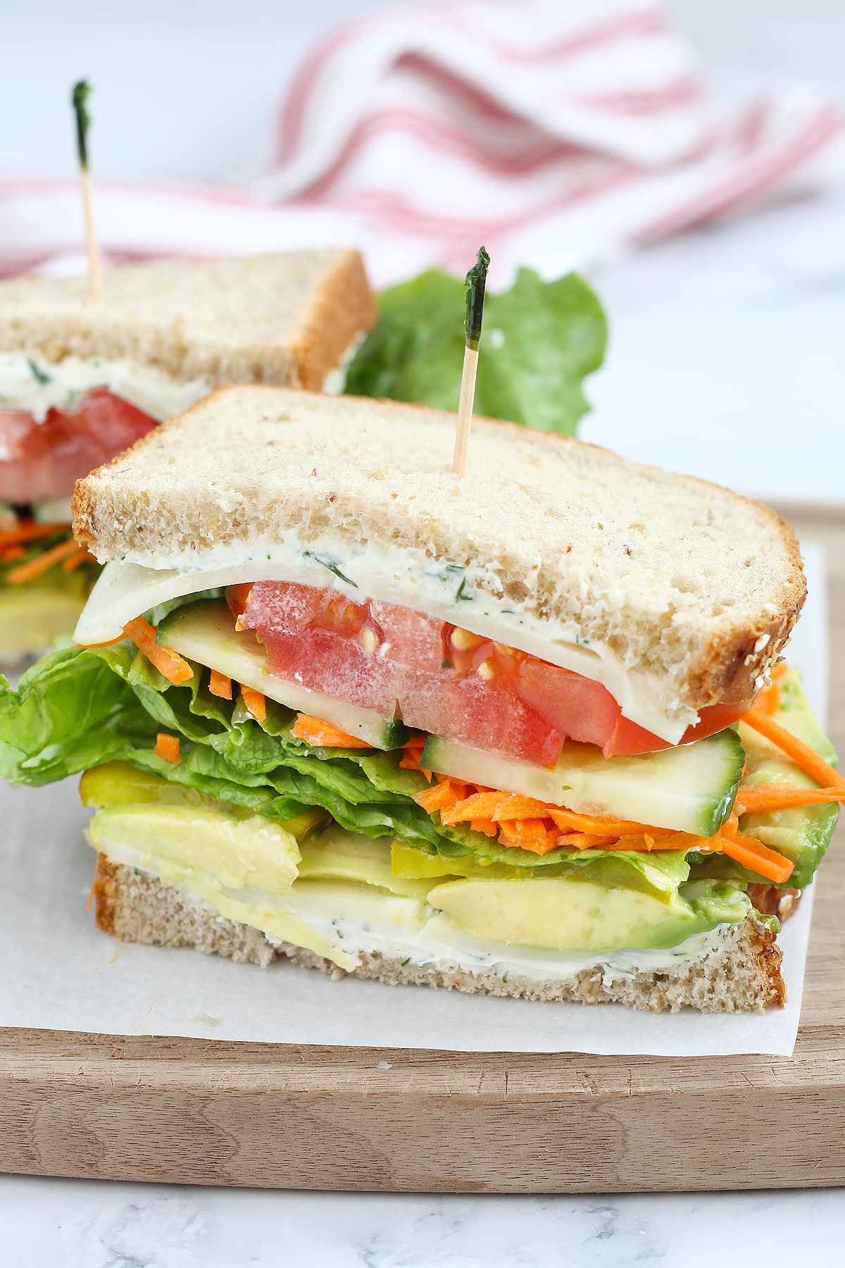 A veggie sandwich on wheat bread with tomatoes, cucumber, lettuce and pickles topped with a frilly toothpick.