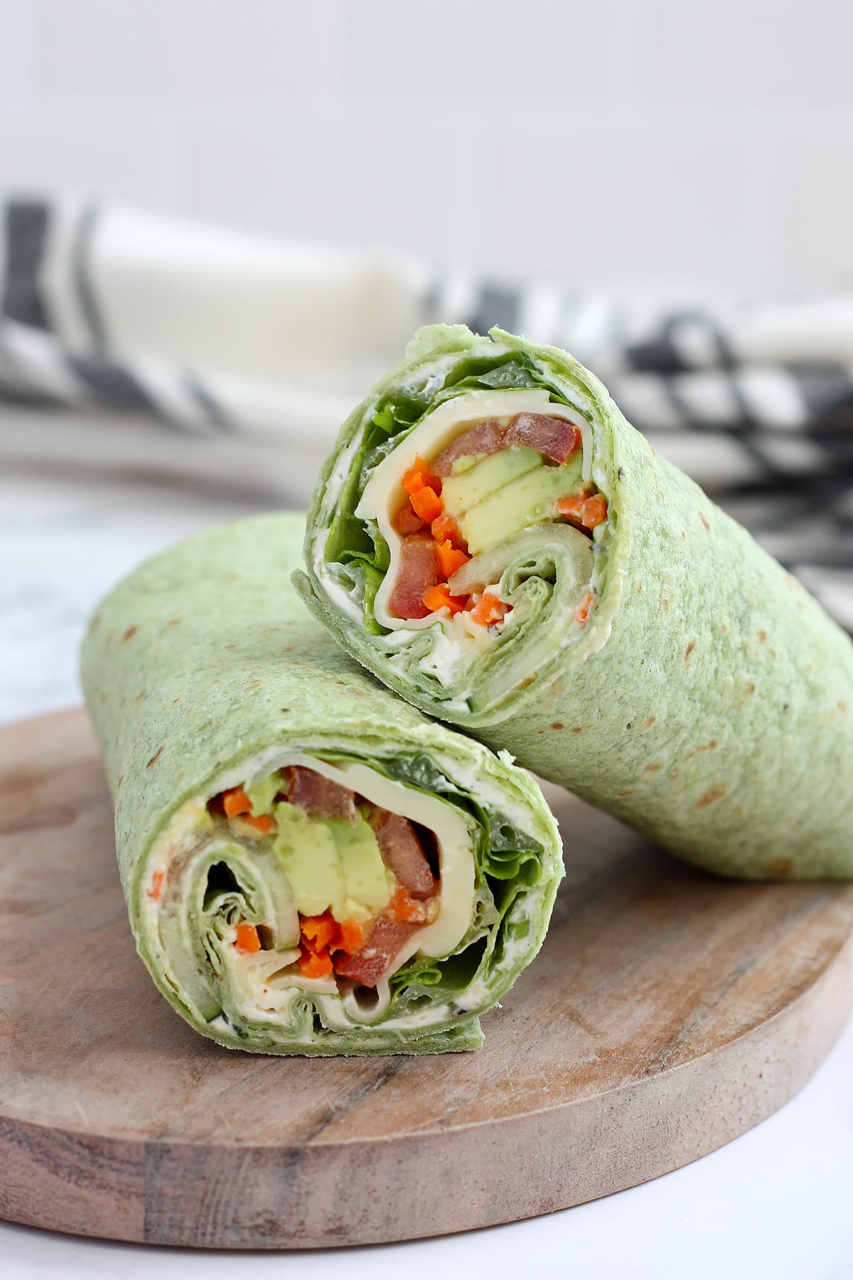 A veggie wrap on a spinach tortilla with cucumbers, tomatoes, and avocados on a wooden cutting board. 