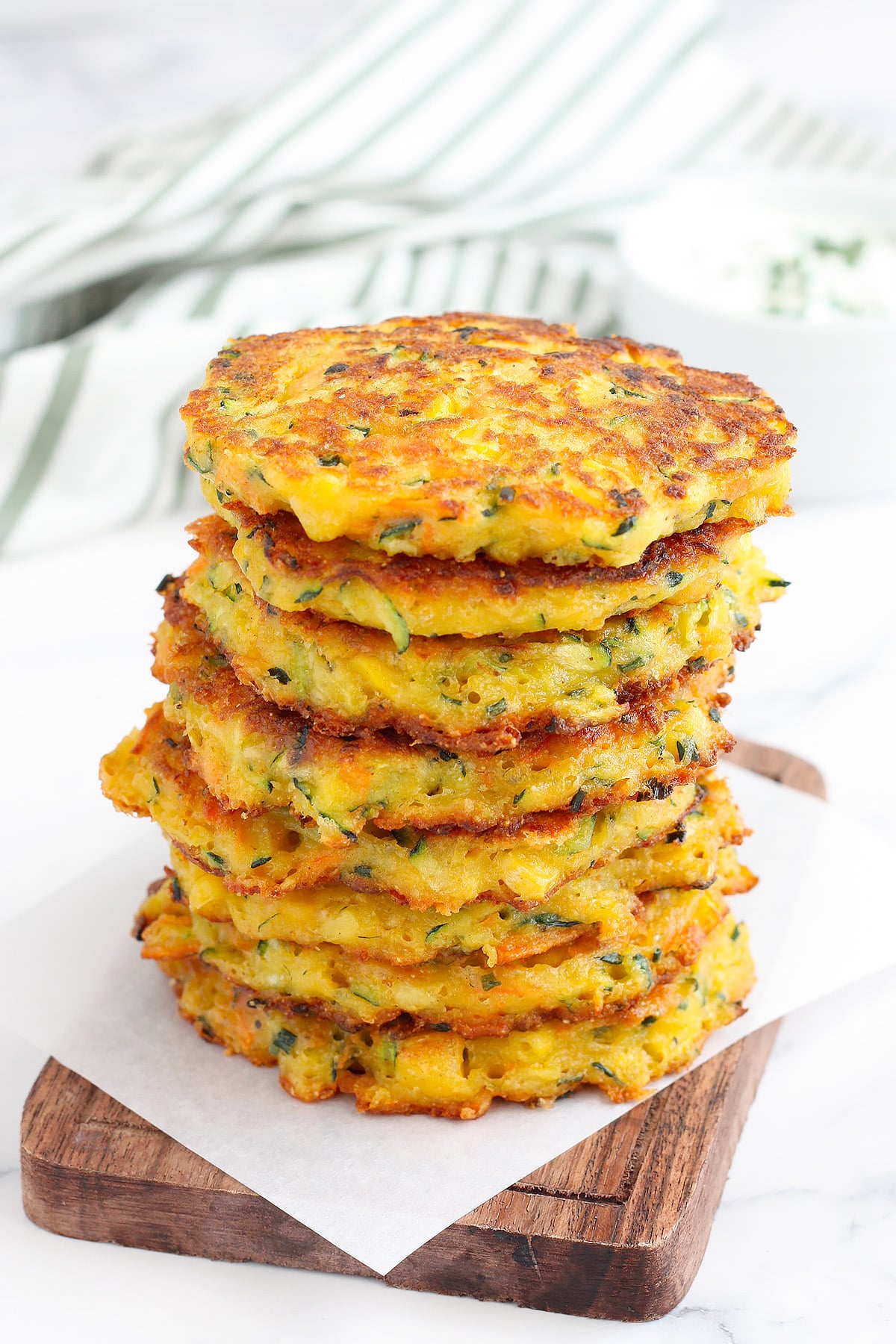 A stack of zucchini fritters on a wooden serving platter with a striped linen in the background. 
