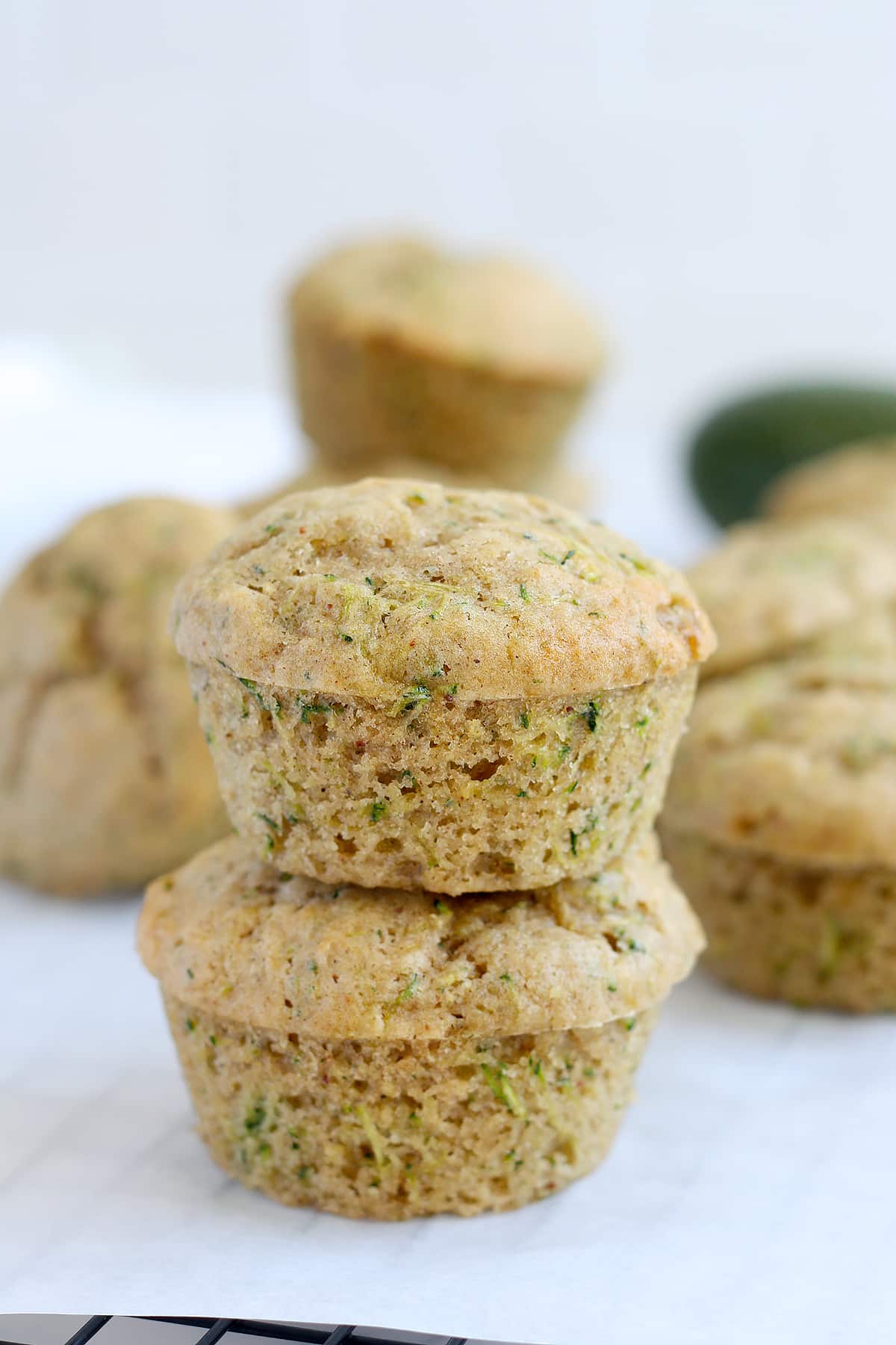 Homemade zucchini muffins, without a liner, stacked one on top of another on a sheet of parchment paper. 