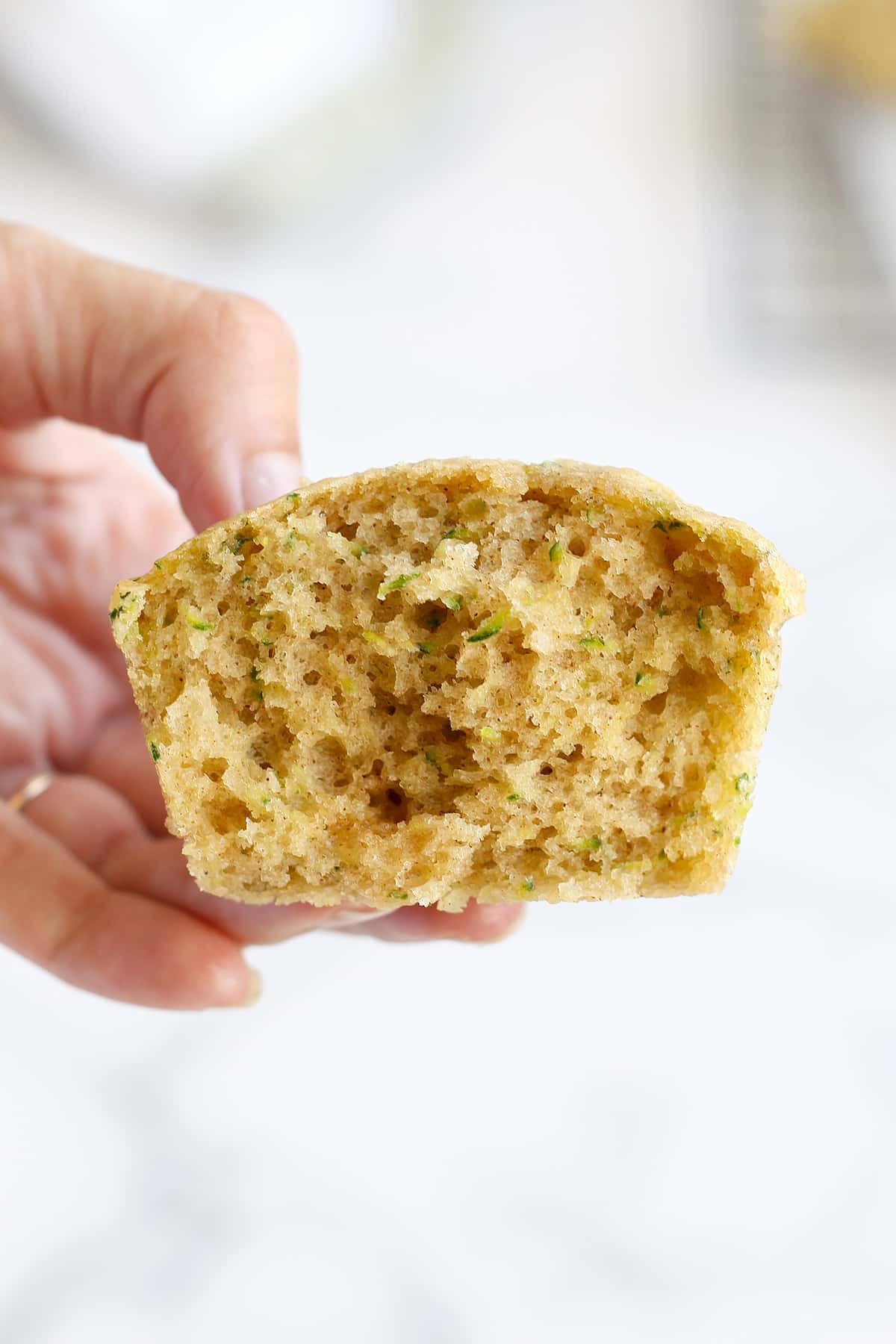 Someone holding half of a zucchini muffin to show the soft texture. 